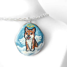 Load image into Gallery viewer, a smooth beach stone, hand painted with a portrait of a shiba inu dog as an angel, sitting on clouds against a light blue sky. available as a keepsake or pendant necklace
