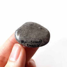 Load image into Gallery viewer, a small smooth beach stone, hand painted with the portrait of an akita dog, painted as an angel, it peers out over fluffy clouds against a blue and pink sky. this piece is available as a keepsake or pendant necklace, back signed with Rainbowofcrazy
