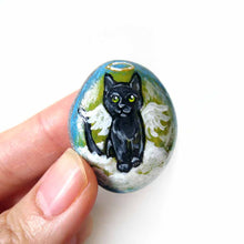 Load image into Gallery viewer, Rock art of a black cat as an angel, painted on a small beach stone, it's available alone, fridge magnet, or as a pendant necklace.
