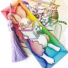 Load image into Gallery viewer, A PET (polyethylene terephthalate) bookmark and purple tassel with a small bead, featuring a character from Rainbow of Crazy Comics reading in a cozy, colourful box: an English spot rabbit reads a book with a ghost holding a camera on the cover. on the side, it says @ Rainbowofcrazy.
