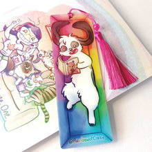 Load image into Gallery viewer, A PET (polyethylene terephthalate) bookmark and red tassel with a small bead, featuring a character from Rainbow of Crazy Comics reading in a cozy, colourful box: a mini lop rabbit reads a book bear holding a hat on the cover. on the bottom, it says @ Rainbowofcrazy.
