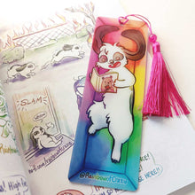 Load image into Gallery viewer, A PET (polyethylene terephthalate) bookmark and red tassel with a small bead, featuring a character from Rainbow of Crazy Comics reading in a cozy, colourful box: a mini lop rabbit reads a book bear holding a hat on the cover. on the bottom, it says @ Rainbowofcrazy.
