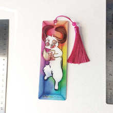 Load image into Gallery viewer, A PET (polyethylene terephthalate) bookmark and red tassel with a small bead, featuring a character from Rainbow of Crazy Comics reading in a cozy, colourful box: a mini lop rabbit reads a book bear holding a hat on the cover. on the bottom, it says @ Rainbowofcrazy.
