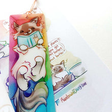 Load image into Gallery viewer, A PET (polyethylene terephthalate) bookmark and orange/yellow tassel, featuring a character from Rainbow of Crazy Comics: a ragdoll cat reads a book with a cat on the cover, as she lounges in a colourful box. on the bottom, it says @ Rainbowofcrazy
