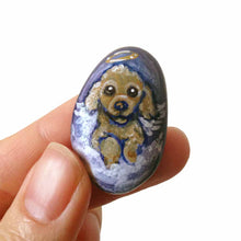 Load image into Gallery viewer, a small beach stone hand painted with the portrait of a brown poodle as an angel, sitting in the clouds against a blue sky. available as a keepsake or pendant necklace
