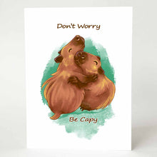 Load image into Gallery viewer, a greeting card with an illustration of two capybaras hugging. the front of the card reads "Don't Worry Be Capy"
