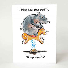 Load image into Gallery viewer, a greeting card with a smiling hippo, riding an orange rocking horse. the card reads, "they see me rollin'. they hatin'"
