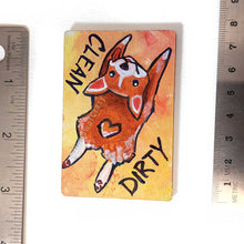 Load image into Gallery viewer, yellow and orange wood magnet, hand painted with a corgi with a tail in a heart shape, tongue out, doing a sploot. near the top of the dog's head is the word CLEAN. written reversed, next to the dog's butt is the word DIRTY
