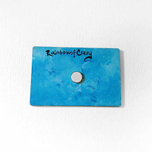 Load image into Gallery viewer, back of a blue wood magnet, with a small magnet in the center. signed with "RainbowofCrazy"

