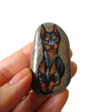 Load image into Gallery viewer, a beach stone hand painted with a portrait of a smiling doberman dog
