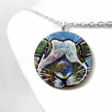 Load image into Gallery viewer, a small round wood disc, hand painted with a portrait of an English Spot rabbit, face up close, painted in rainbow colours. it's available as a keepsake or pendant necklace
