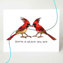 Load image into Gallery viewer, a greeting card featuring an illustration of two cardinals, beaks just touching. it reads, "Home is where you are". the image has a flowing line through the card, showing colour options of red (male) cardinals or tan (female) cardinals
