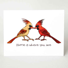 Load image into Gallery viewer, a greeting card featuring an illustration of two cardinals, one female, one male, beaks just touching. it reads, "Home is where you are".
