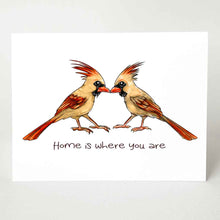 Load image into Gallery viewer, a greeting card featuring an illustration of two cardinals, two female, beaks just touching. it reads, "Home is where you are". 
