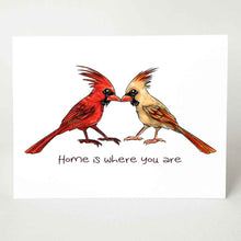 Load image into Gallery viewer, a greeting card featuring an illustration of two cardinals, one male, one female, beaks just touching. it reads, "Home is where you are".
