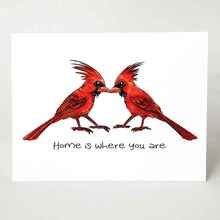 Load image into Gallery viewer, a greeting card featuring an illustration of two cardinals, both male, beaks just touching. it reads, "Home is where you are".
