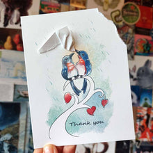 Load image into Gallery viewer, holding up a handmade greeting card wtih an illustration of two bluebirds on a tree branch. the top right corner of the card is ripped off and hangs from one bluebird's mouth, as it holds it up above the other bird, protecting it from the rain. the card says, "thank you"
