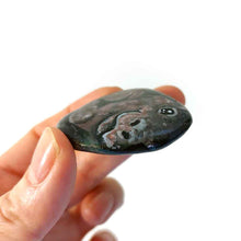 Load image into Gallery viewer, a hand holding a smooth, flat, beach stone hand painted with a smiling hippo
