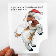 Load image into Gallery viewer, a funny greeting card with a goat on the front, wearing a christmas hat, with the bottom right corner of the card ripped and hanging from its mouth. the card reads, "I got you a Christmas card but  I eated it"
