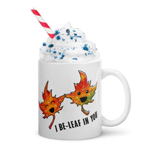 Load image into Gallery viewer, A 11 oz white ceramic mug, printed with art of two maple leaves with happy faces, and the words. "I be-leaf in you"
