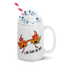 Load image into Gallery viewer, A 15 oz white ceramic mug, printed with art of two maple leaves with happy faces, and the words. "I be-leaf in you"
