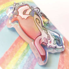 Load image into Gallery viewer, A clear, blue-tinted holographic acrylic keychain featuring a character from Rainbow of Crazy Comics: an English spot rabbit, lying down, admires a potted plant. 
