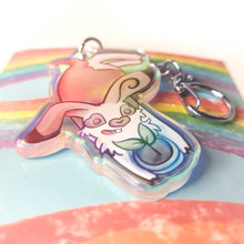 Load image into Gallery viewer, A clear, blue-tinted holographic acrylic keychain featuring a character from Rainbow of Crazy Comics: an English spot rabbit, lying down, admires a potted plant. 
