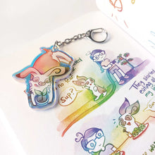 Load image into Gallery viewer, A clear, blue-tinted holographic acrylic keychain featuring a character from Rainbow of Crazy Comics: an English spot rabbit, lying down, admires a potted plant. 
