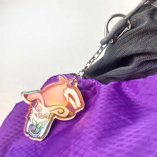 Load image into Gallery viewer, A clear, blue-tinted holographic acrylic keychain featuring a character from Rainbow of Crazy Comics: an English spot rabbit, lying down, admires a potted plant. 
