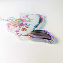 Load image into Gallery viewer, A clear, rainbow holographic acrylic keychain featuring a character from Rainbow of Crazy Comics: a smiling mini lop rabbit lounges on his back as he reads a book with a picture of a rabbit on the back. Shown at a different angle.
