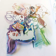 Load image into Gallery viewer, A clear, rainbow holographic acrylic keychain featuring a character from Rainbow of Crazy Comics: a smiling mini lop rabbit lounges on his back as he reads a book with a picture of a rabbit on the back. Shown next to an illustration of characters from the comics.
