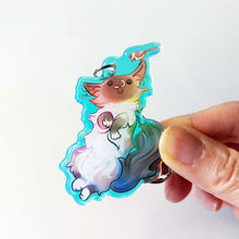 Load image into Gallery viewer, A clear, rainbow holographic acrylic keychain featuring a character from Rainbow of Crazy Comics: a smiling fluffy ragdoll cat, lying on her back, with a tiny black-capped chickadee, the bird perched on the cat's ear.
