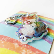 Load image into Gallery viewer, A clear, rainbow holographic acrylic keychain featuring a character from Rainbow of Crazy Comics: a smiling fluffy ragdoll cat, lying on her back, with a tiny black-capped chickadee, the bird perched on the cat's ear.
