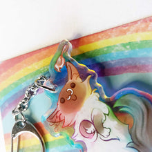 Load image into Gallery viewer, close-up of a clear, rainbow holographic acrylic keychain featuring a character from Rainbow of Crazy Comics: a smiling fluffy ragdoll cat, lying on her back, with a tiny black-capped chickadee, the bird perched on the cat's ear.

