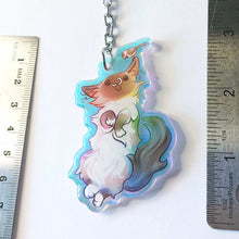 Load image into Gallery viewer, A clear, rainbow holographic acrylic keychain featuring a character from Rainbow of Crazy Comics: a smiling fluffy ragdoll cat, lying on her back, with a tiny black-capped chickadee, the bird perched on the cat's ear.

