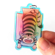 Load image into Gallery viewer, A clear, rainbow holographic acrylic keychain featuring a character from Rainbow of Crazy Comics: a smiling tabby cat lounges in a cardboard box.
