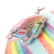 Load image into Gallery viewer, A clear, blue tinted holographic acrylic keychain featuring a character from Rainbow of Crazy Comics: a smiling tabby cat lounges in a cardboard box.
