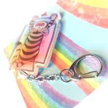 Load image into Gallery viewer, A clear, blue tinted holographic acrylic keychain featuring a character from Rainbow of Crazy Comics: a smiling tabby cat lounges in a cardboard box.
