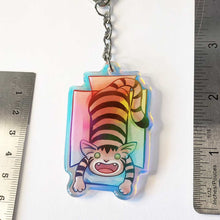 Load image into Gallery viewer, A clear, blue tinted holographic acrylic keychain featuring a character from Rainbow of Crazy Comics: a smiling tabby cat lounges in a cardboard box.
