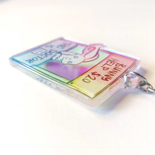 Load image into Gallery viewer, Side view of a clear, rainbow holographic acrylic keychain featuring a character from Rainbow of a Crazy Comics: a smiling white rabbit at a homemade booth that says "bunny help $20" at the top, and "the doctor is in" at the bottom. 
