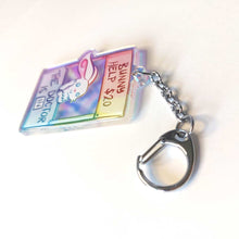 Load image into Gallery viewer, A clear, rainbow holographic acrylic keychain featuring a character from Rainbow of a Crazy Comics: a smiling white rabbit at a homemade booth that says "bunny help $20" at the top, and "the doctor is in" at the bottom. 
