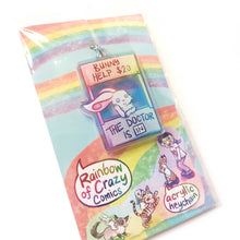 Load image into Gallery viewer, A clear, rainbow holographic acrylic keychain featuring a character from Rainbow of a Crazy Comics: a smiling white rabbit at a homemade booth that says "bunny help $20" at the top, and "the doctor is in" at the bottom.  The keychain is packaged with a backing card, decorated with a rainbow, and the text "Rainbow of Crazy Comics", along with the character cast.
