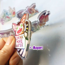 Load image into Gallery viewer, A hand holds up the cat acrylic magnet, showing a small magnet embedded in the acrylic on the side of the piece.
