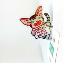 Load image into Gallery viewer, An acrylic magnet featuring a character from Rainbow of Crazy Comics: a cat smiles and holds up a sign that says "DRINK MORE WATER". The magnet stands perpendicular to the magnetic surface, making it look like the character is peeking out at you. The magnet holds up a small print.
