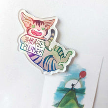Load image into Gallery viewer, An acrylic magnet featuring a character from Rainbow of Crazy Comics: a tabby cat smiles and holds up a sign that says "HYDRATE PLEASE?!". The Magnet holds up a small print of a black cat sitting on top of a hill, holding a red balloon.
