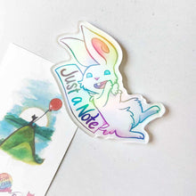 Load image into Gallery viewer, An acrylic magnet featuring a character from Rainbow of Crazy Comics: a white rabbit smiles next to a sign that says "Just a Note". The Magnet holds up a small print of a black cat sitting on top of a hill, holding a red balloon.

