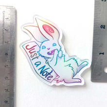 Load image into Gallery viewer, An acrylic magnet featuring a character from Rainbow of Crazy Comics: a white rabbit smiles next to a sign that says "Just a Note". The Magnet holds up a small print of a black cat sitting on top of a hill, holding a red balloon. The magnet is next to rulers, showing its length at about 2.5"
