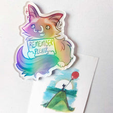 Load image into Gallery viewer, An acrylic magnet featuring a character from Rainbow of Crazy Comics: a ragdoll cat smiles and holds up a sign that says "REMEMBER PLEASE". The Magnet holds up a small print of a black cat sitting on top of a hill, holding a red balloon.
