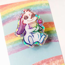 Load image into Gallery viewer, An acrylic pin featuring a character from Rainbow of Crazy Comics: a mini lop rabbit hugging a book, with a tiny heart next to him.
