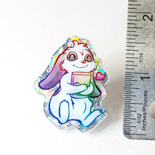 Load image into Gallery viewer, A glittery acrylic pin featuring a character from Rainbow of Crazy Comics: a mini lop rabbit hugging a book, with a tiny heart next to him.
